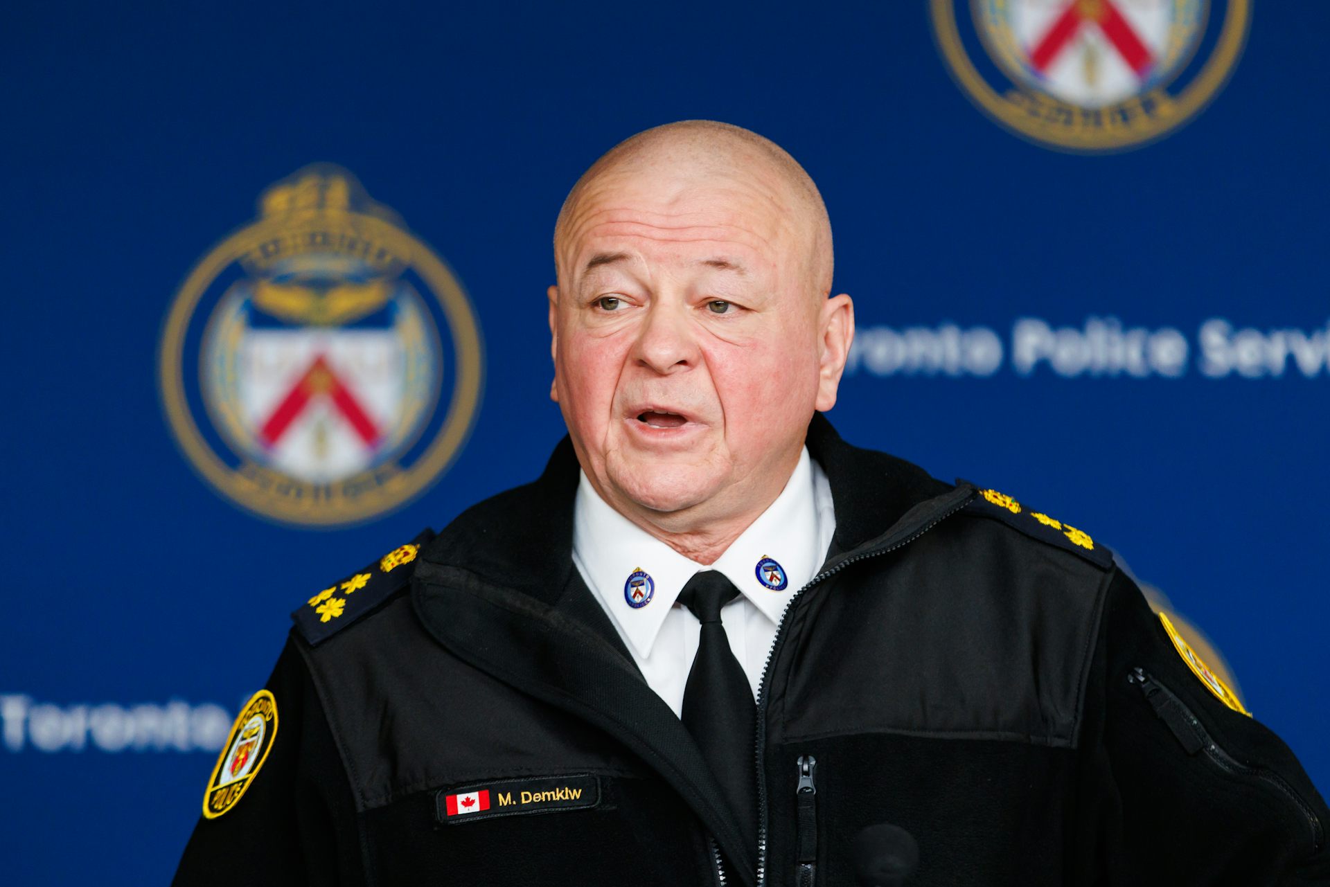 An older bald man in an uniform at a news conference.