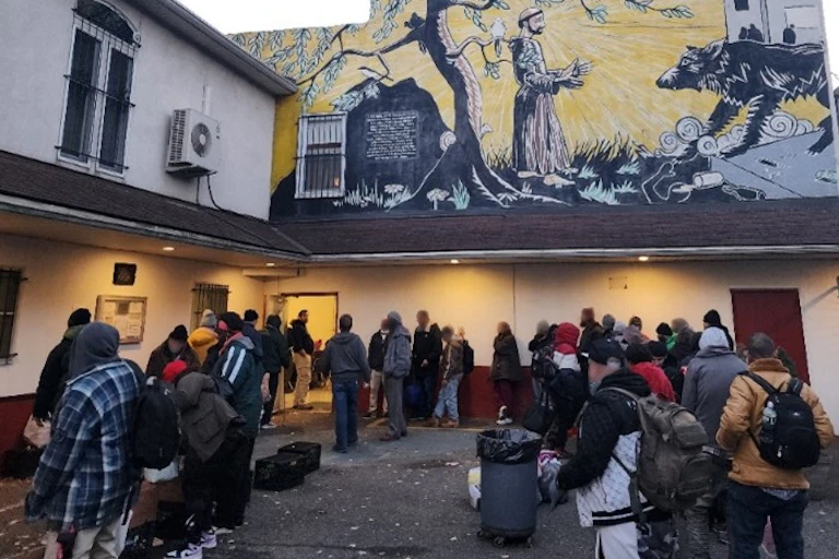 Large group of people gather outside a building with a religious mural