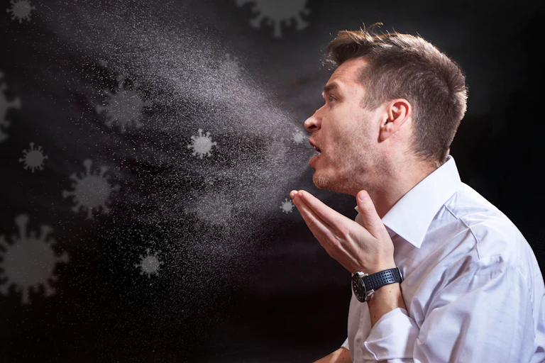 Une illustration montre un homme qui tousse et émet des particules virales dans l'air.