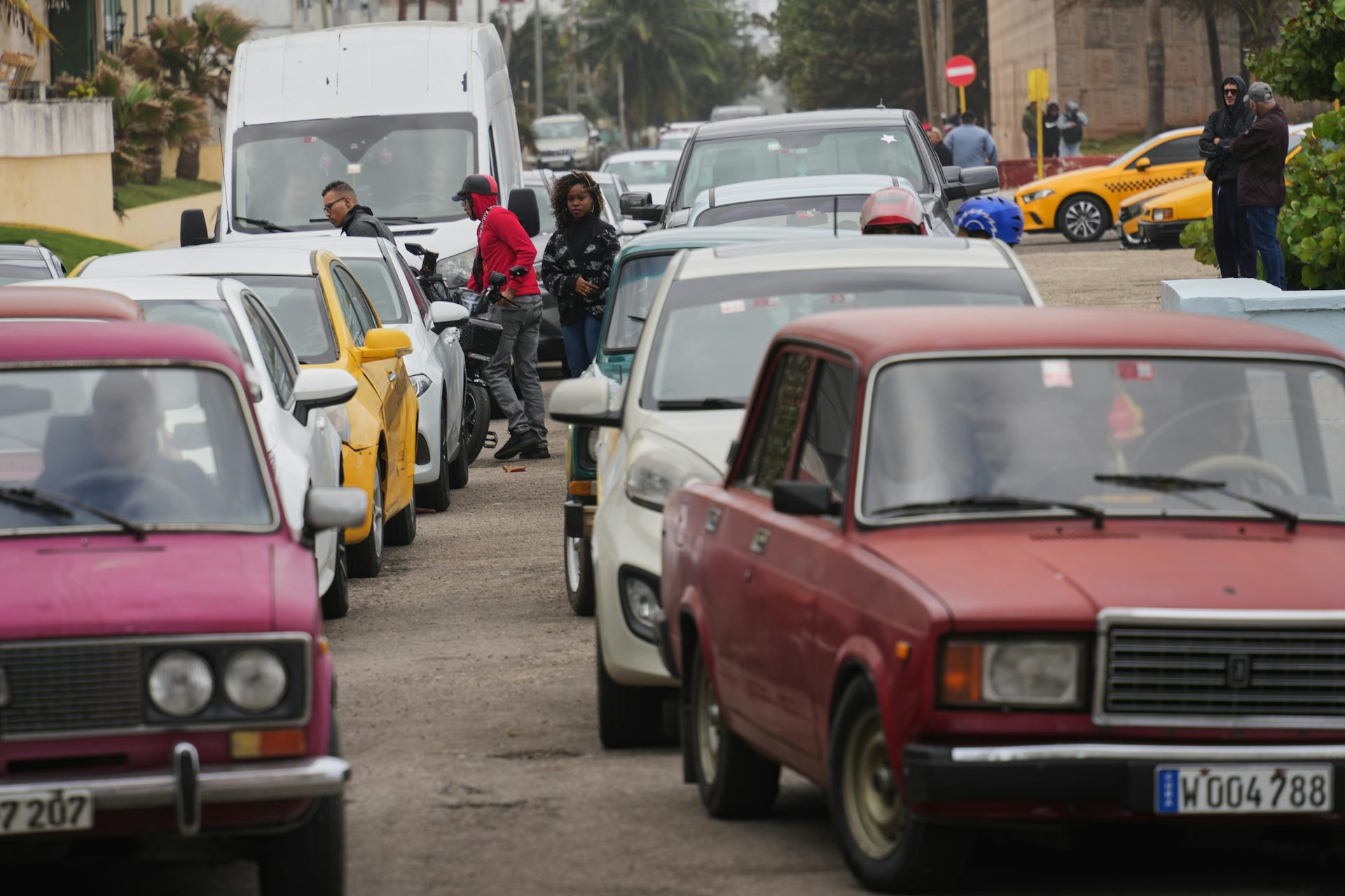 Drivers in a long line of colourful cars, some from the 1950s, waiting to fill up.