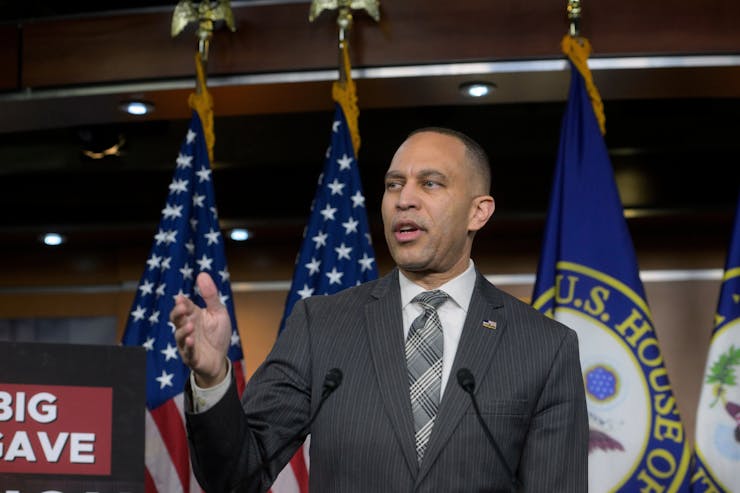 Standing in front of U.S. and congressional flags, Rep. Hakeem Jeffries gestures with his right hand.