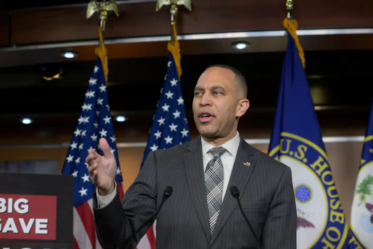 Standing in front of U.S. and congressional flags, Rep. Hakeem Jeffries gestures with his right hand.