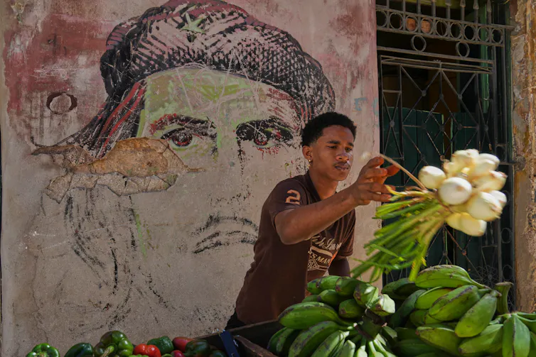 Un jeune homme tient un paquet d’oignons devant une fresque murale représentant Che Guevara