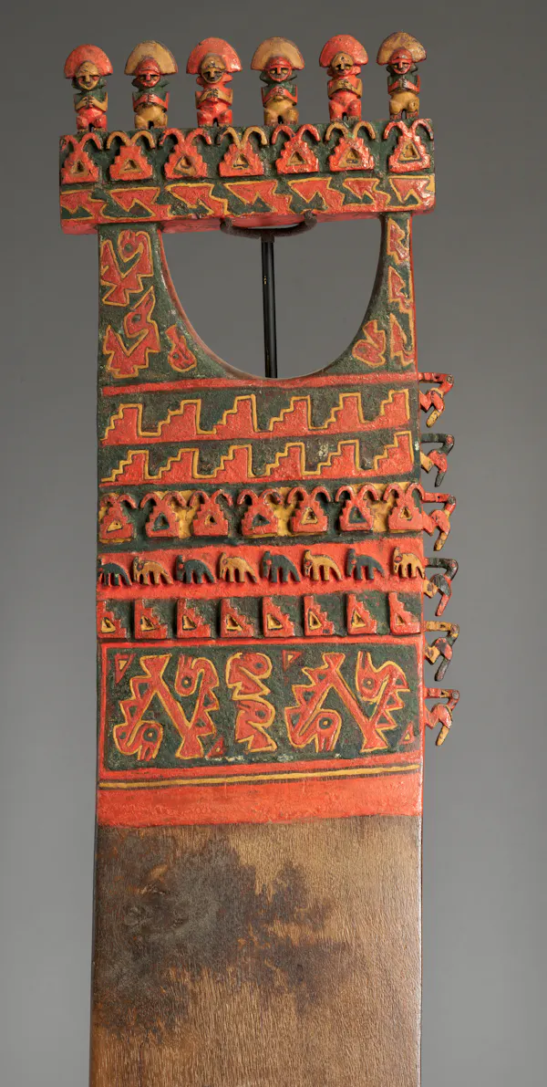 Remo de madera tallada decorada con pintura roja, verde y amarilla, con una línea de pequeñas figuras en la parte superior y tallas de animales en el centro.
