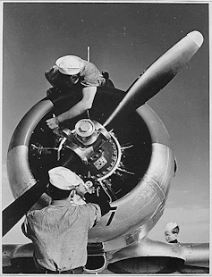 Two military mechanics work on the propeller engine of an aircraft.