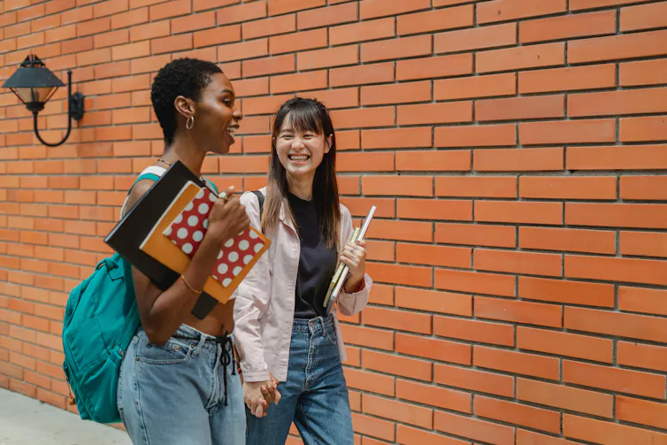 Two teen girls in a hallway who are laughing.