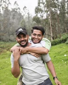 One youth is hugging another youth from behind and both are laughing.