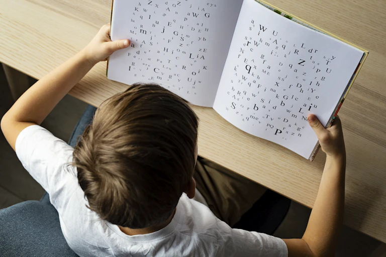 A boy is seen from behind reading a book that has jumbled words on it.
