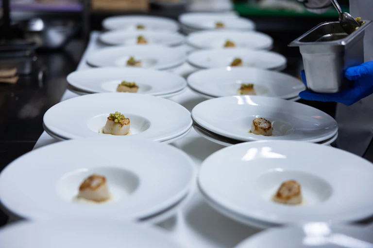 white plates lined up in a restaurant with a single scallop on each