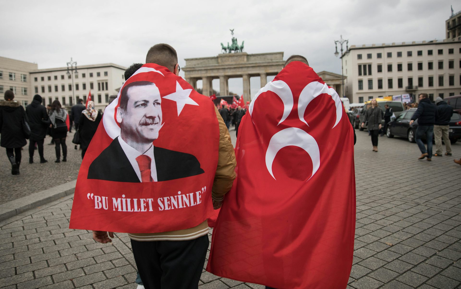 Two men wearing red flags with a man's face on them.