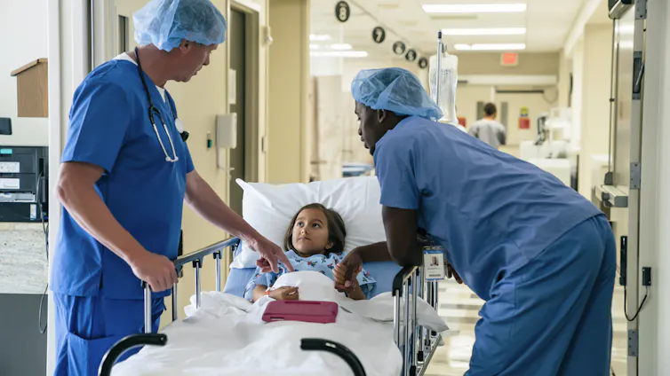 Two health care workers speak with a child lying on a hospital gurney