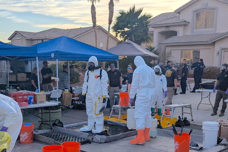 People in biohazard suits standing in the driveway of a suburban home.