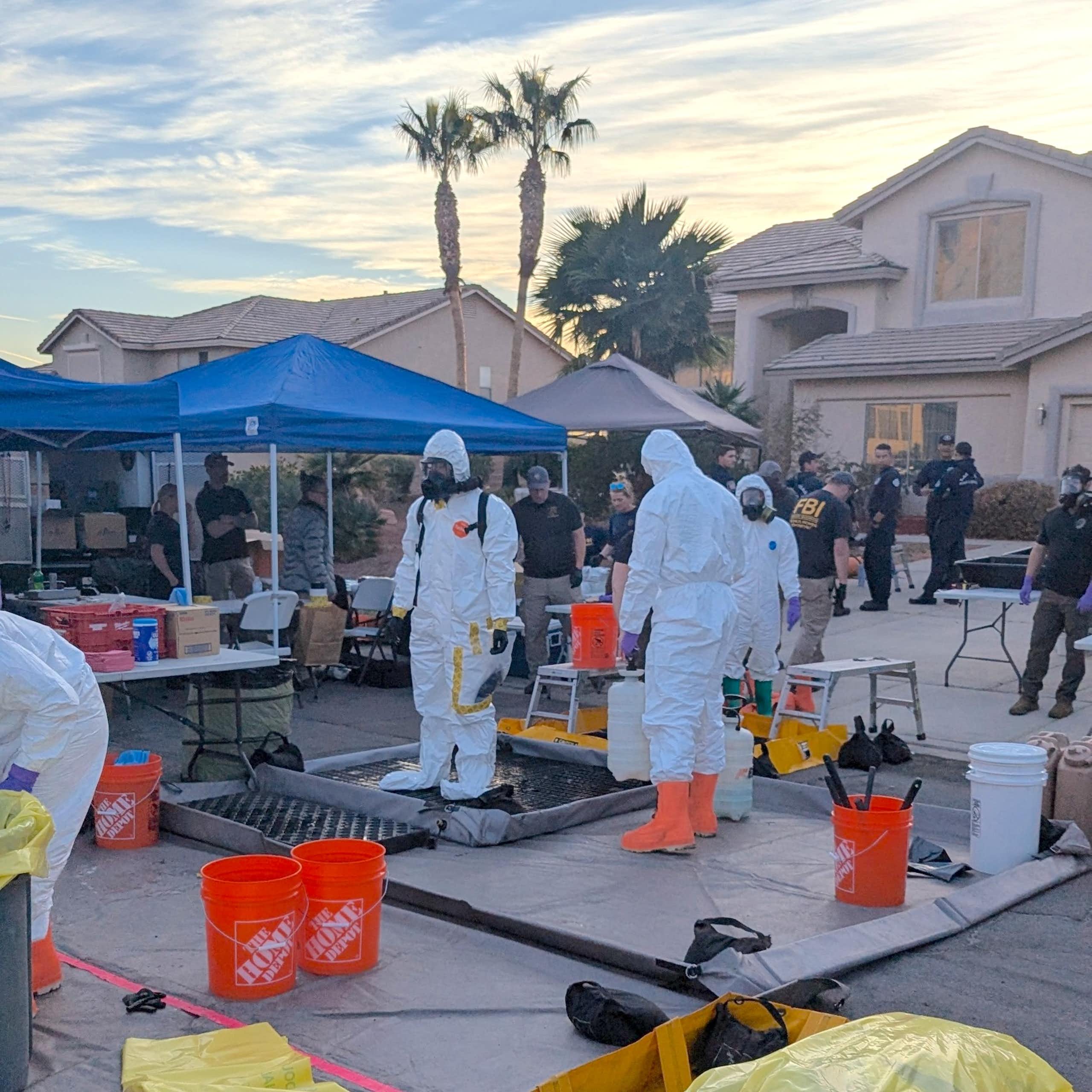 People in biohazard suits standing in the driveway of a suburban home.