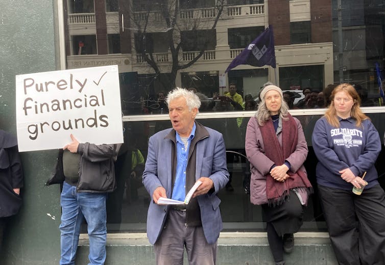 a man with a sign 'purely for financial grounds', a man reading, two other people