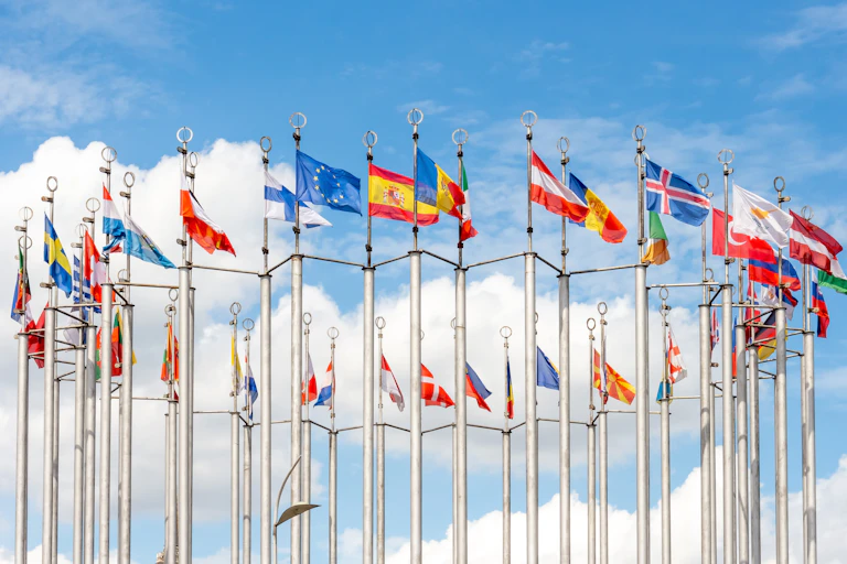 Banderas de países ondean contra el cielo azul con pocas nubes.