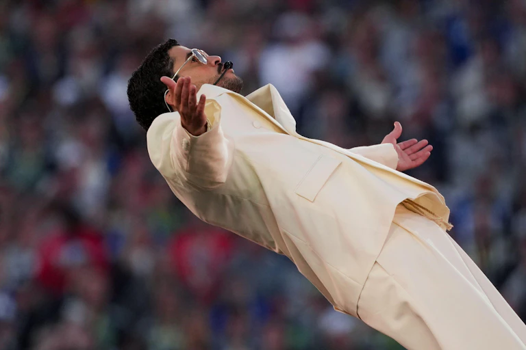 A man dressed in a cream suit and sunglasses soaks up the adoration of a concert crowd on stage.