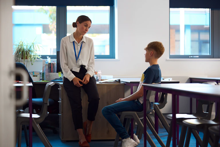 Teacher talking to pupil in empty classroom