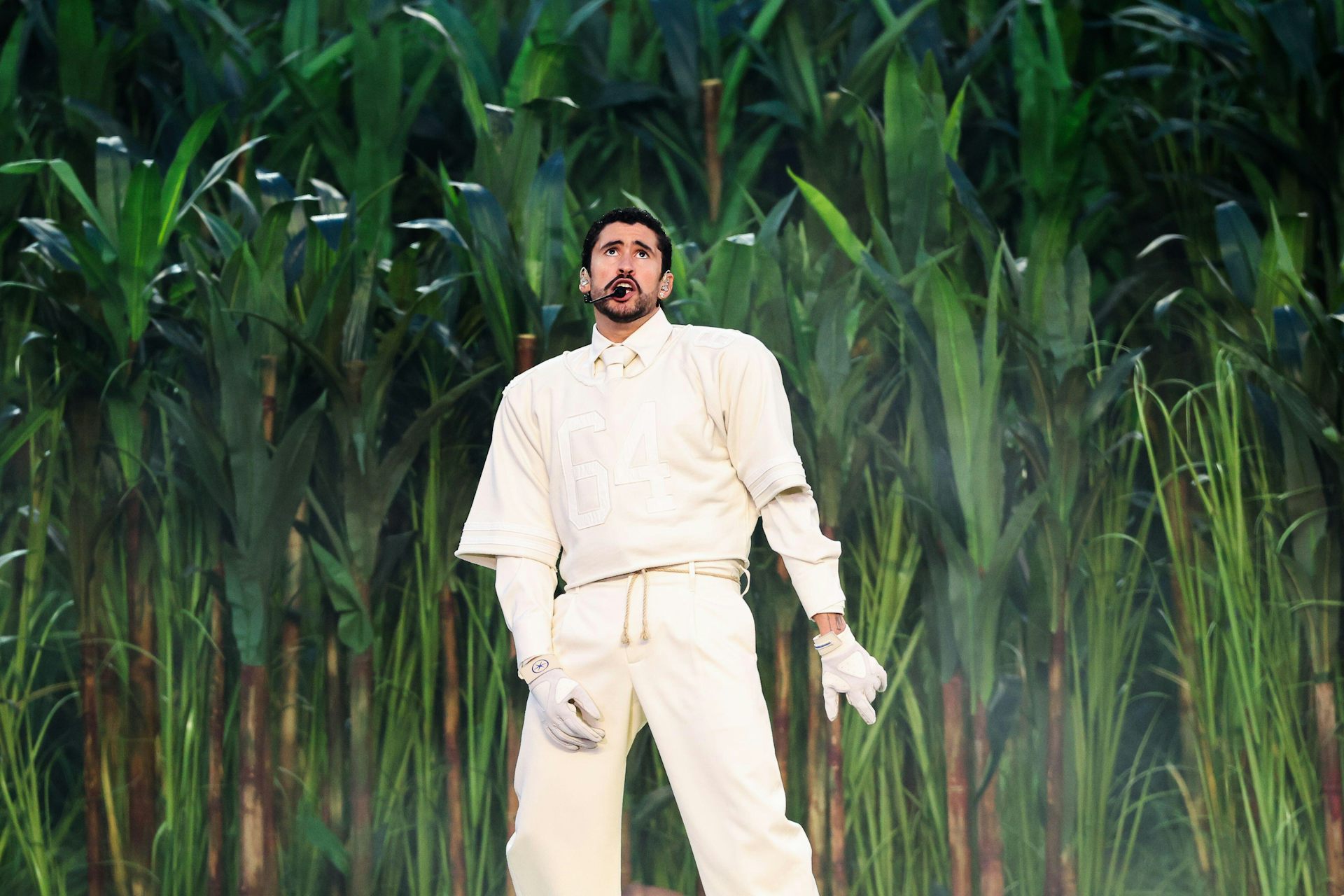 A man dressed in cream on the Super Bowl halftime stage, with a crop of sugar cane behind him.
