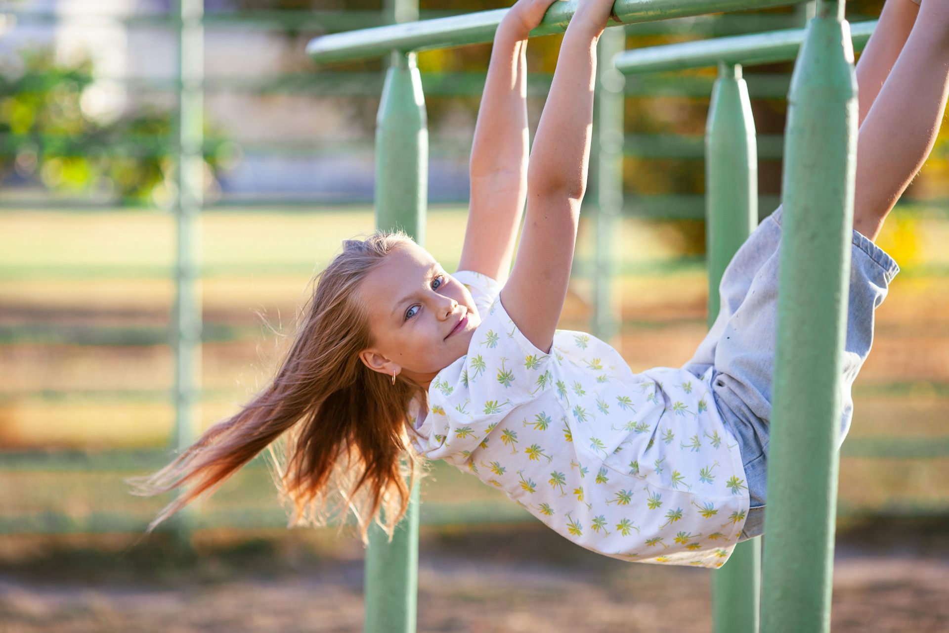 Blond girl hangs from monkey bars.