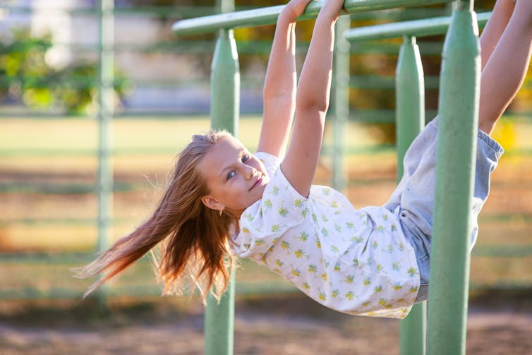 Blond girl hangs from monkey bars.