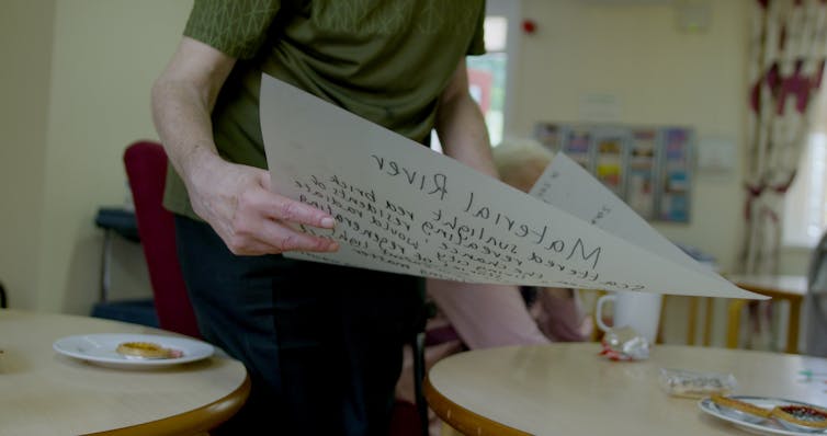 woman holds page of paper with poetry text over tables