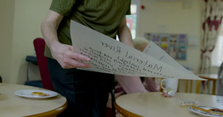 woman holds page of paper with poetry text over tables