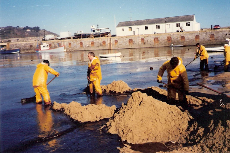 people in yellow waterproofs cleaning up oily foreshore by Welsh village