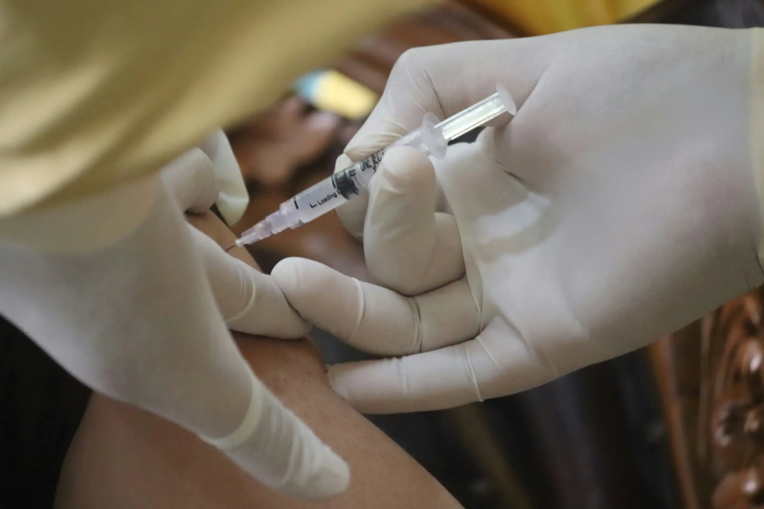 Two gloved hands vaccinating someone.