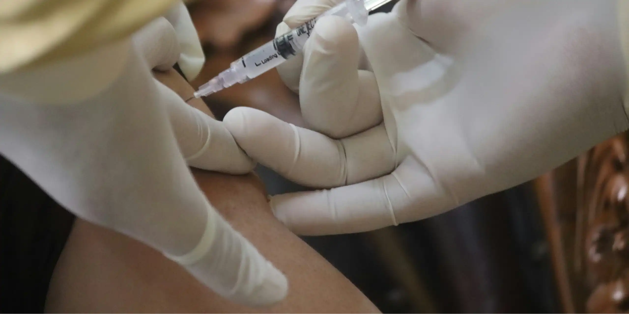 Two gloved hands vaccinating someone.