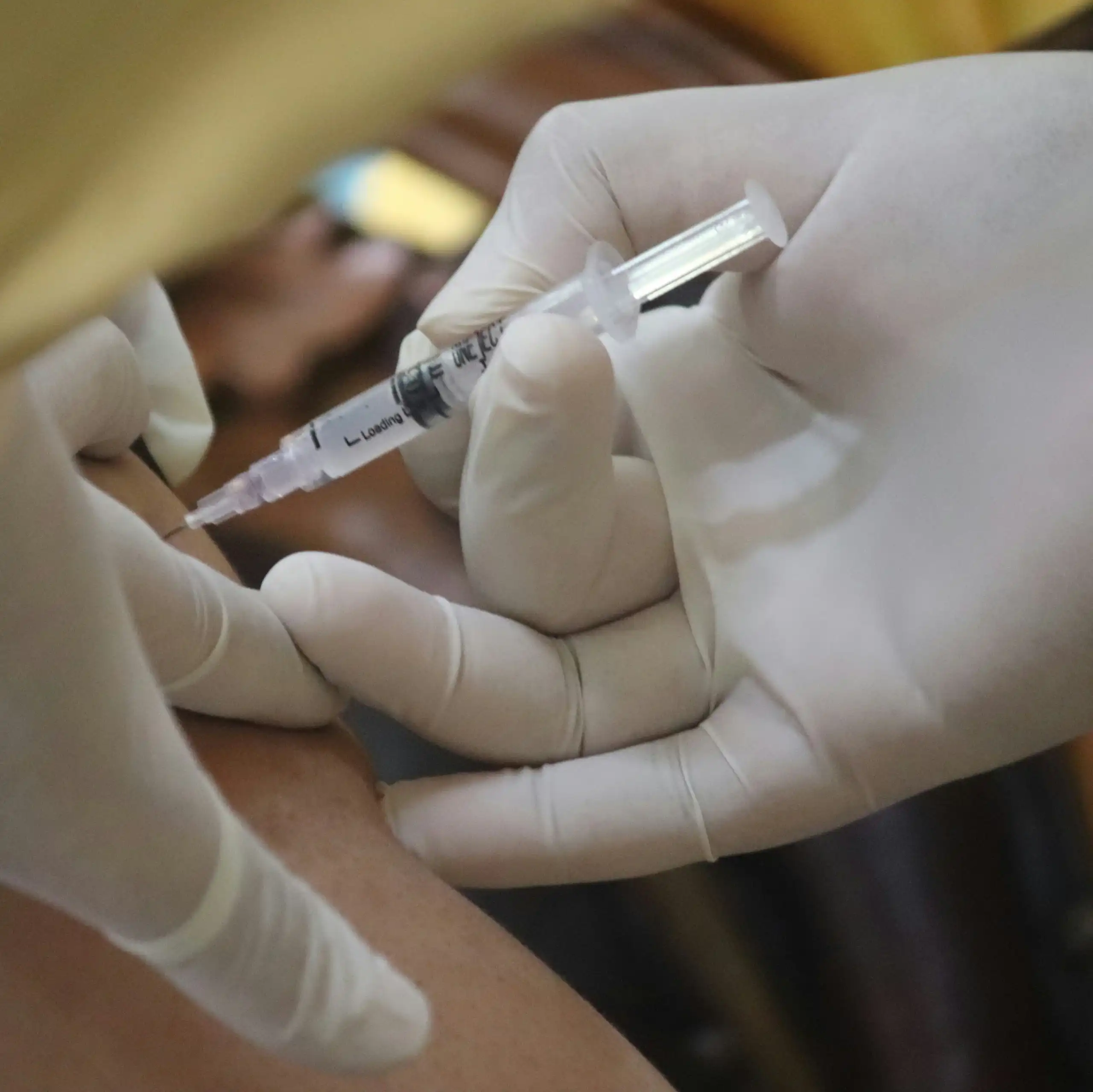 Two gloved hands vaccinating someone.