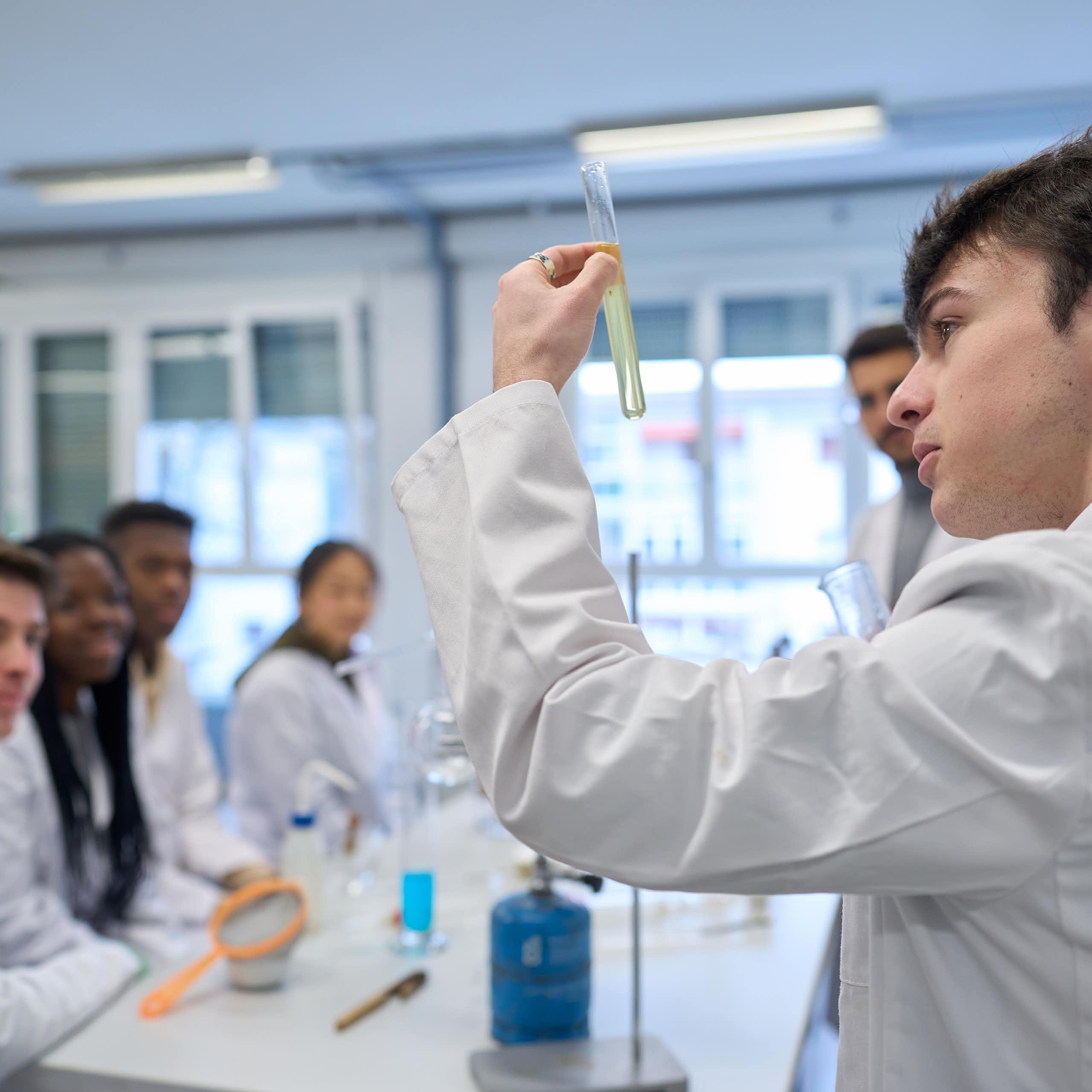 Un jove amb bata blanca mira una proveta.