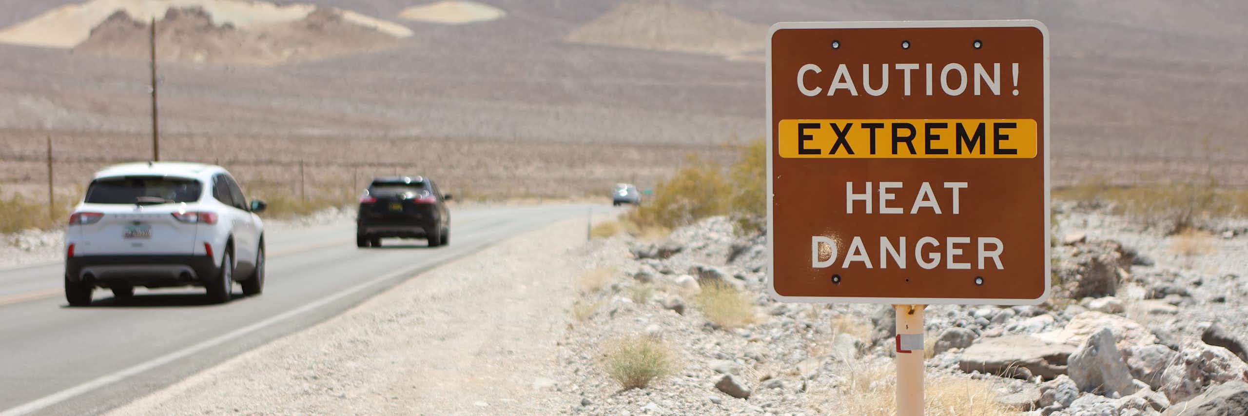 Cars drive past a sign reading 'Caution: Extreme Heat Danger'