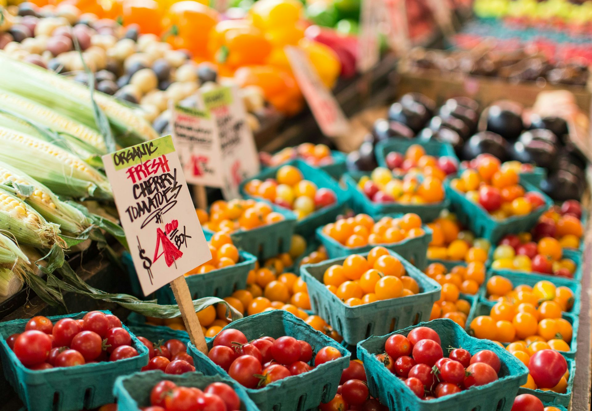 Mercado de agricultores con cajas de tomates cherry orgánicos y mazorcas de maíz.