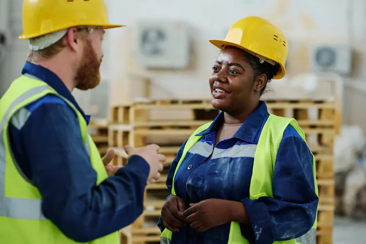 Two construction workers in hard hats converse while smiling