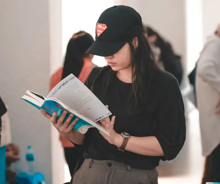woman standing and reading book, cap over eyes, long hair
