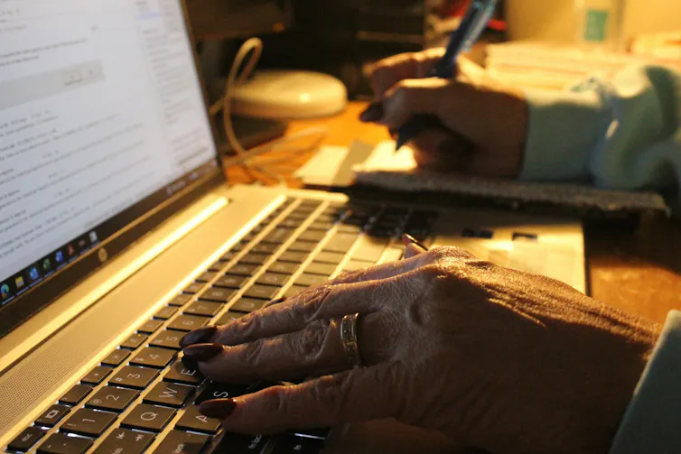 close up on one hand on laptop keyboard and other hand writing next to laptop