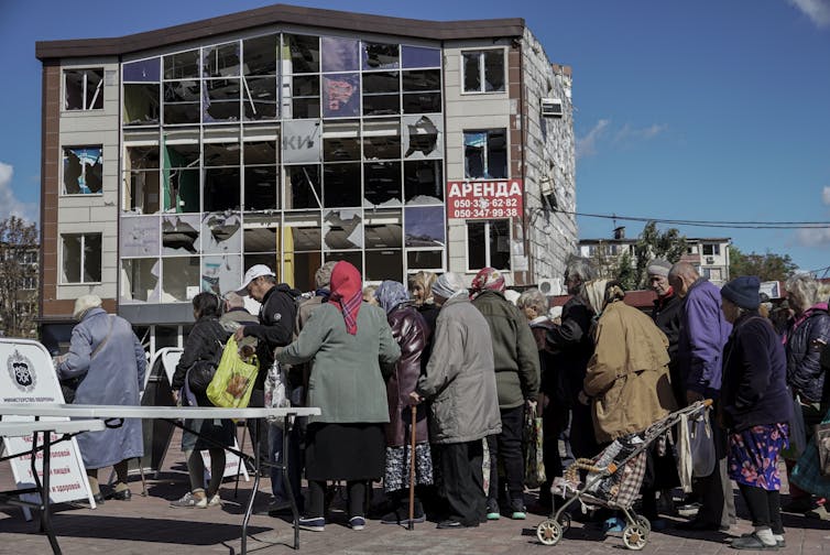A line of Ukrainians waits to vote in front of a bomb-damaged apartment building, September 2022.