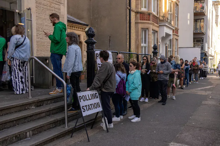 Queue of people outside building with polling station sign