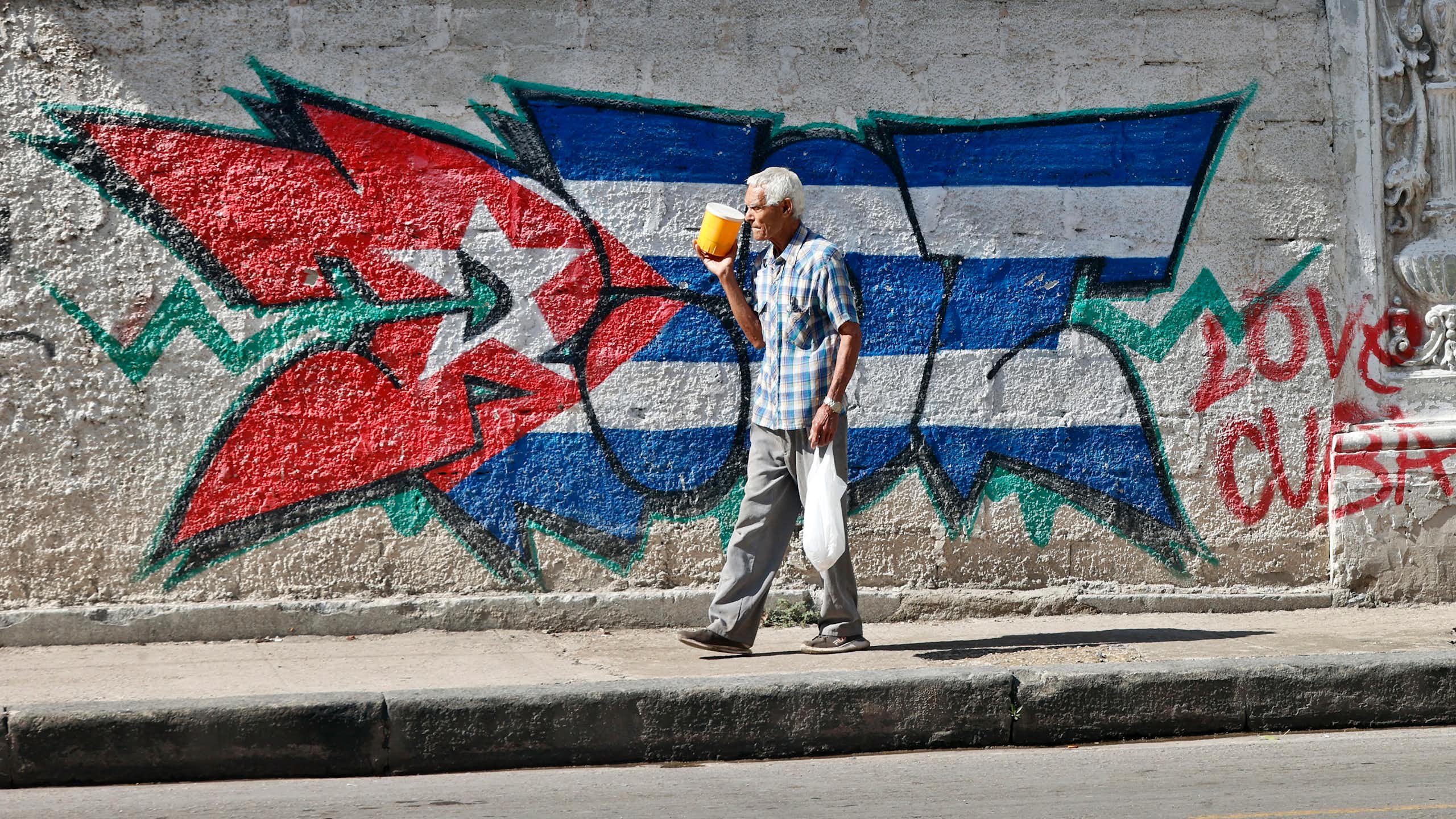 A person walks past a Cuban flag on a street in Havana.