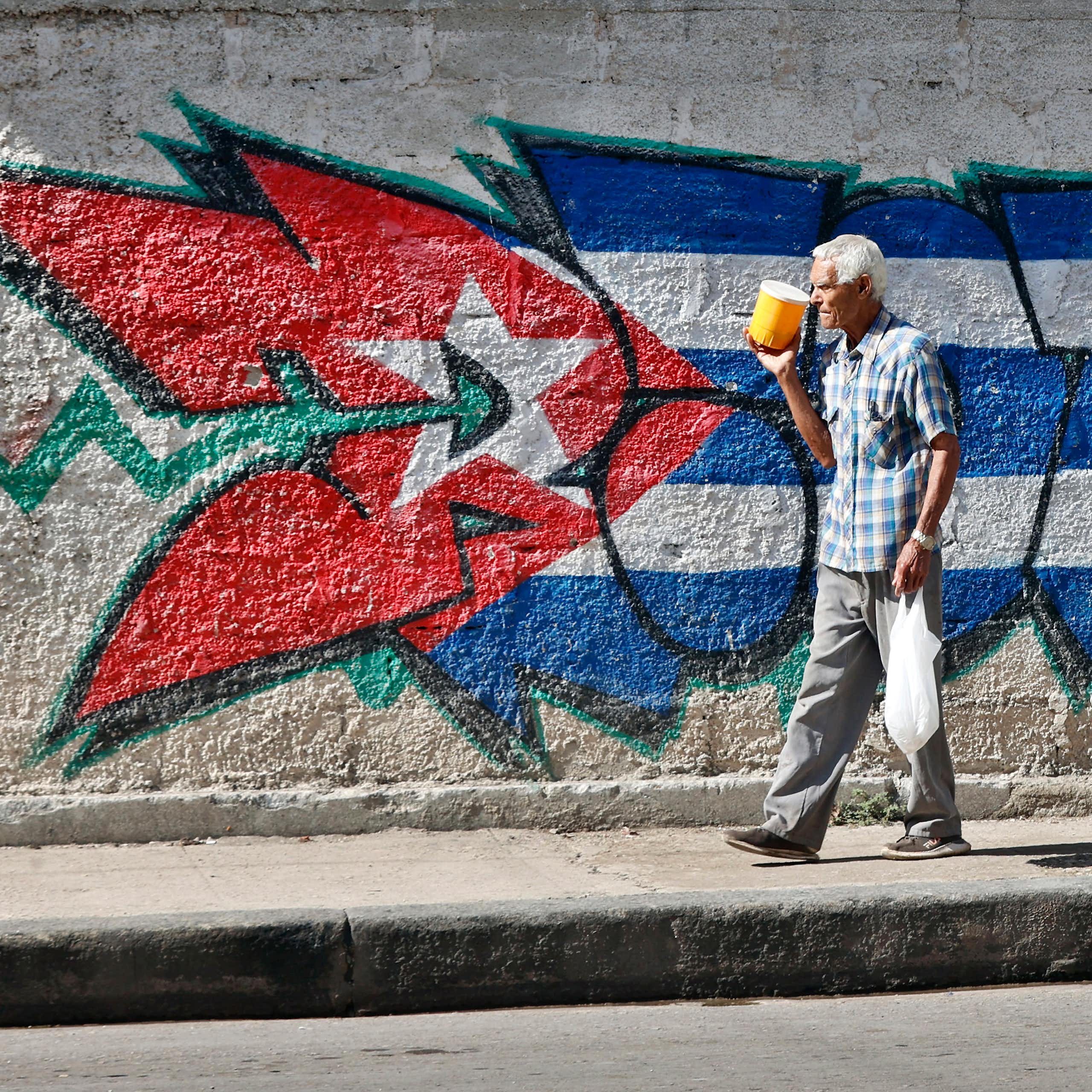 A person walks past a Cuban flag on a street in Havana.
