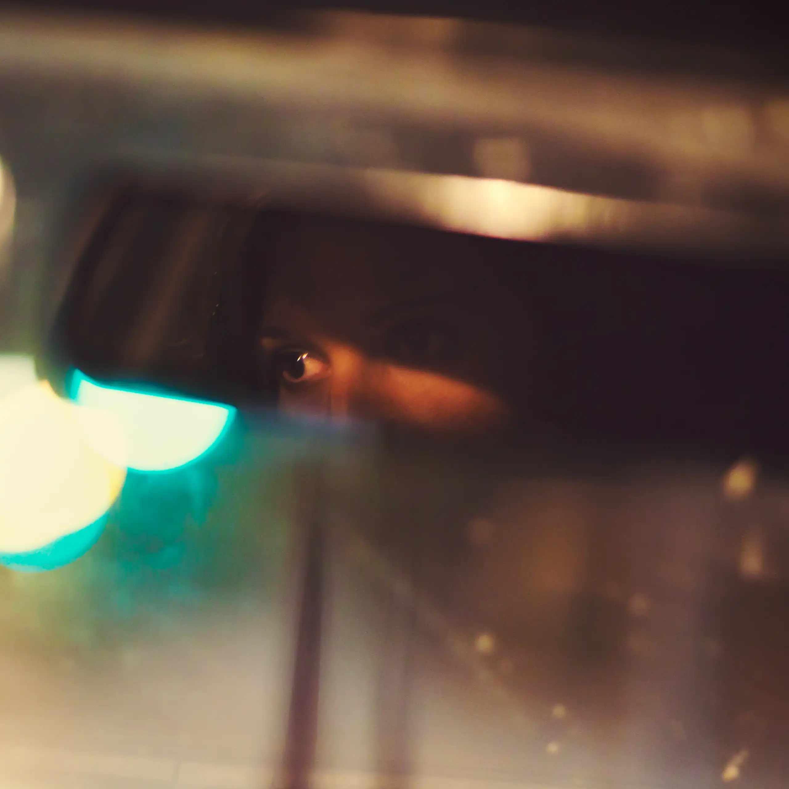 A woman drives a car at night with her eyes visible through the rearview mirror.