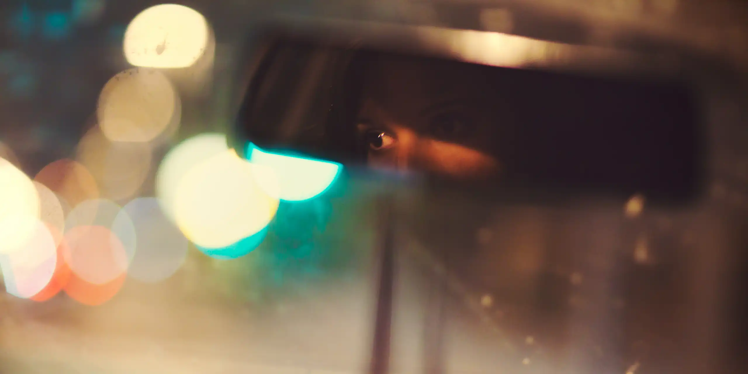 A woman drives a car at night with her eyes visible through the rearview mirror.