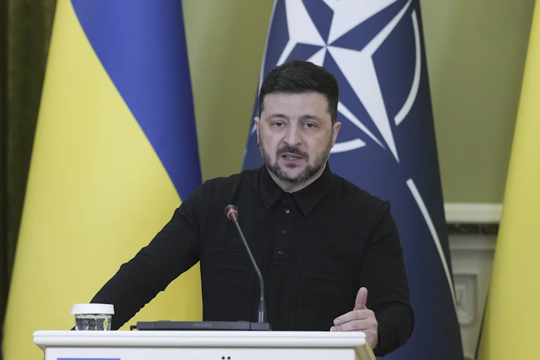 Ukrainian president, Volodymyr Zelensky, stands at a podium in front of a Ukranian flag.