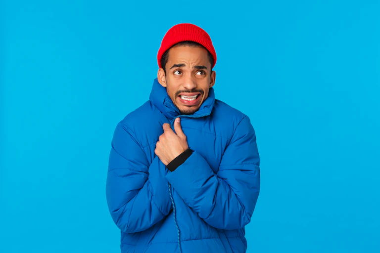 Man wearing red hat and blue puffa jacket against blue background.