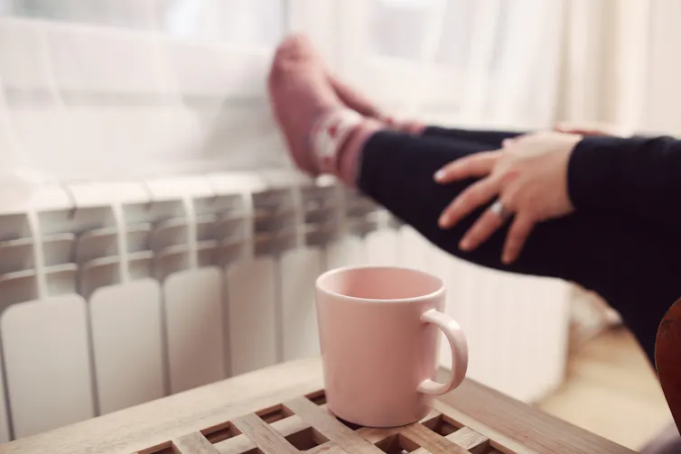 Woman sits with pink mug and feet against radiator