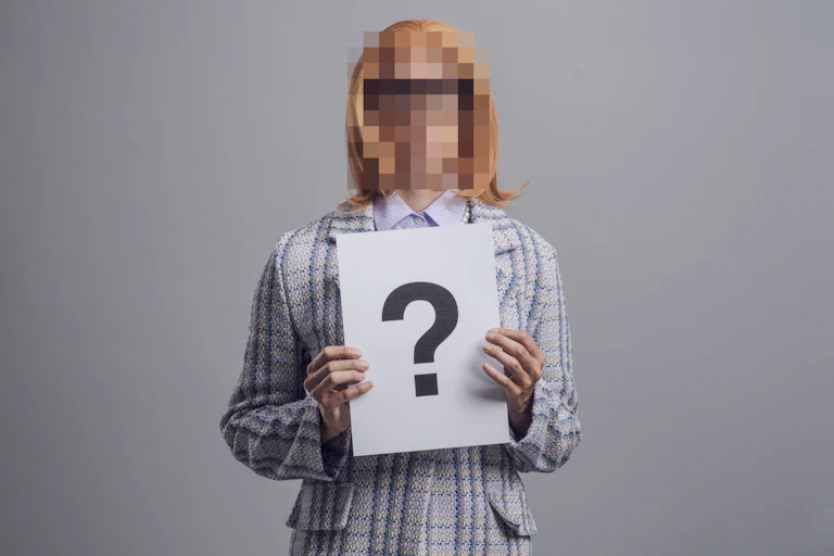 Una mujer con la cara pixelada sostiene una cartulina con un interrogante.