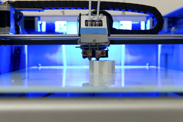 The inside of a 3D printer where a piece deposits a thin stream of material onto a round part.