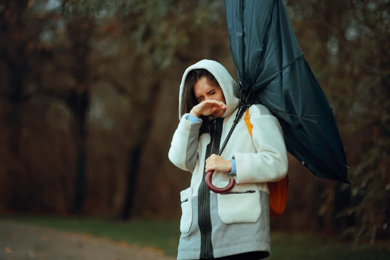 A woman with broken umbrella looks depressed during a rainstorm.