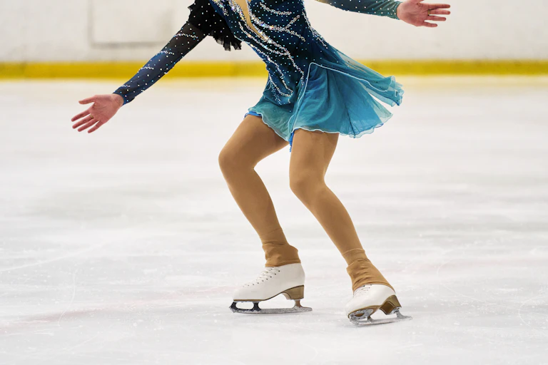 Side view of the legs of a young woman in a dress and skirt practicing ice figure skating.