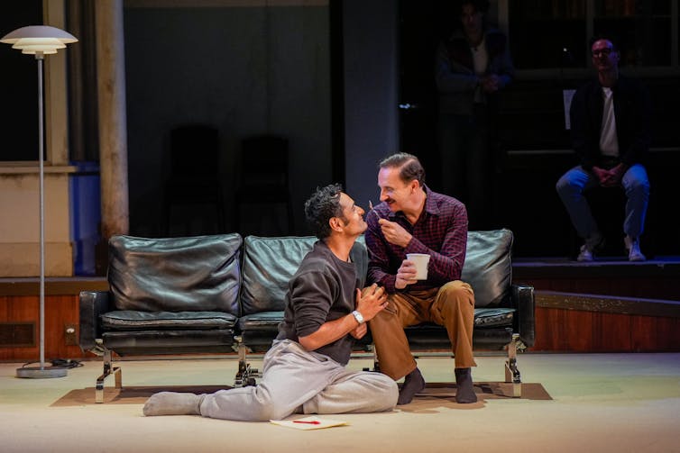 Production image: two men are close on a couch.